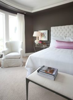 a white bed sitting in a bedroom next to a chair and table with a book on it