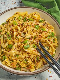 a bowl filled with noodles and vegetables on top of a table next to chopsticks