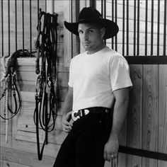 a man wearing a cowboy hat standing in front of a horse stall with his hands on his hips