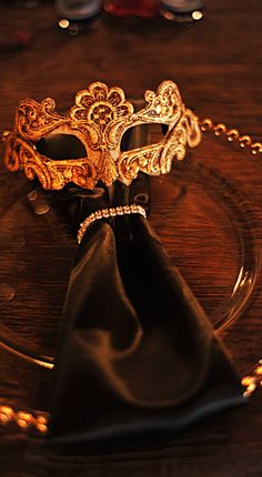 a fancy mask on a glass plate with a black napkin and gold chain around it