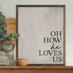 a wooden sign that says oh how he loves us on it next to a vase with flowers