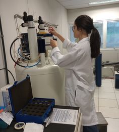 a woman in white lab coat standing next to a machine and looking at something on the table