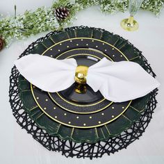 a black and gold place setting with white napkins on the plate, pine cones in the background