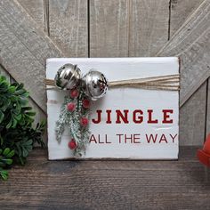 a wooden sign that says jungle all the way with bells and holly on it next to a potted plant