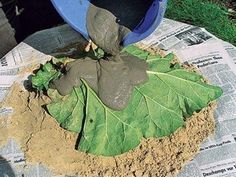 a blue bucket filled with dirt next to a green leaf on top of a newspaper