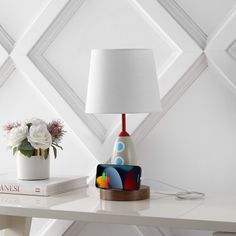 a white table with a lamp and some flowers on it next to a bookshelf