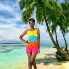 a woman standing on top of a sandy beach next to palm trees and the ocean