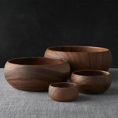 three wooden bowls sitting next to each other on a gray tableclothed surface with black walls in the background