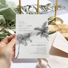 a person holding up a wedding card with palm trees on it