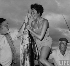 an old black and white photo of a woman holding a fish while two men look on