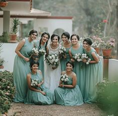 a group of women standing next to each other in front of some bushes and flowers