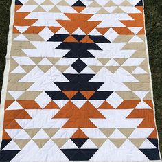 an orange, black and white quilt on the ground with grass in the foreground