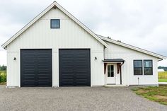 a white house with two black garage doors on it's side and gravel driveway