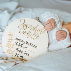 a baby laying on top of a white bed next to a wooden plaque that says someone's company