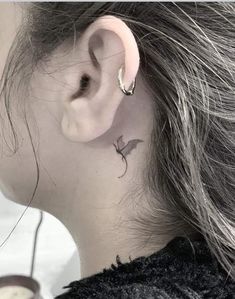 a woman's left ear has a small bird tattoo on it