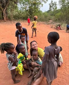 a group of young children sitting on top of a red dirt field next to each other