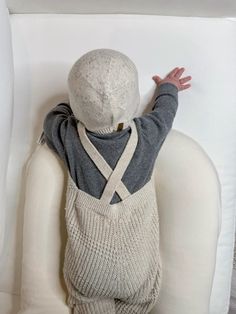 a little boy sitting on top of a white chair wearing a sweater and suspenders