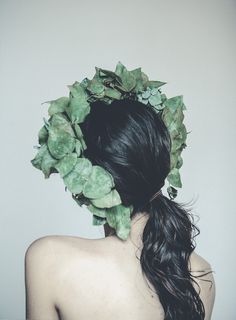 a woman with long black hair wearing a leafy wreath around her head and back to the camera