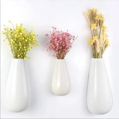 three white vases with yellow and pink flowers in them against a white wall background