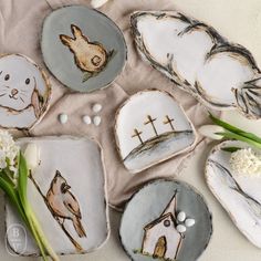 several plates with animals painted on them sitting next to flowers and seashells in the sand