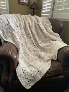 a white crocheted blanket sitting on top of a brown leather couch next to a window