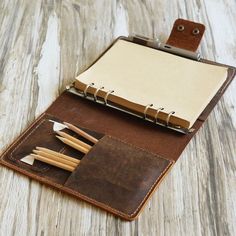 an open notebook with pencils in it on a wooden table