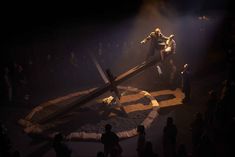 people standing on top of a cross in the middle of a stage with lights coming from behind it