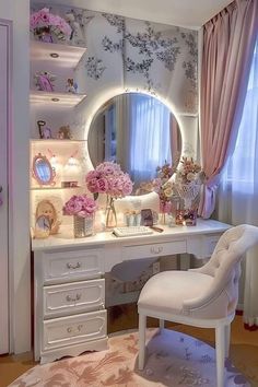 a white vanity with flowers on it and a chair in front of the mirror that is lit up