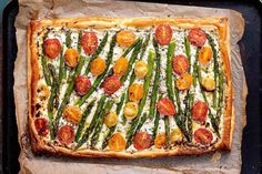 a square pizza with asparagus, tomatoes and cheese on it sitting on a baking sheet