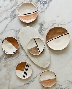 five white and gold plates on a marble counter top with black lines painted on them