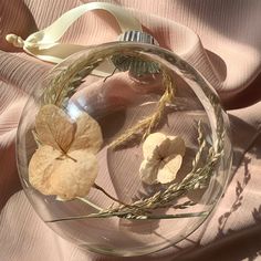 a glass ornament with dried flowers in it on a pink cloth covered surface