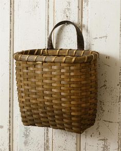 a woven basket hanging on a white wooden wall with an iron hook in the corner