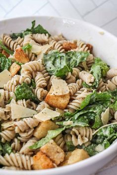 a white bowl filled with pasta and spinach on top of a marble countertop