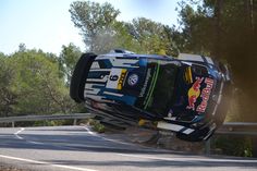 a car that is upside down on the side of a road with trees in the background