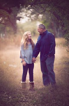 a man and woman holding hands while standing in the middle of a field with trees