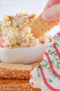 a person dipping crackers into a bowl of dip with sprinkles and candy canes