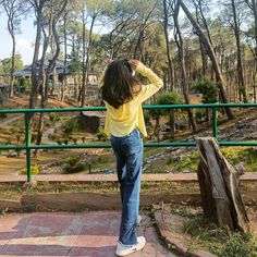 a woman in yellow shirt and jeans looking at trees