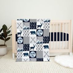 a baby crib with a bear, deer and arrow quilt in the center next to a plant