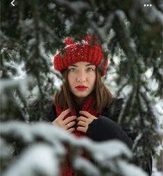 a woman wearing a red hat and scarf standing in front of snow covered pine trees