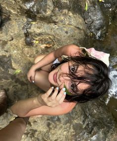 a young woman sitting on top of a rock next to a river holding a cell phone