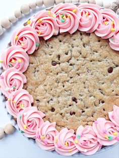 a cookie cake with pink frosting and sprinkles on top, surrounded by cookies