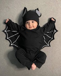 a baby dressed in a bat costume laying on the floor with his hands up and eyes closed