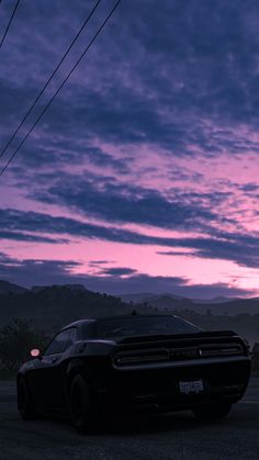 a black car parked on the side of a road at dusk with mountains in the background