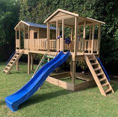 a wooden playset with a blue slide in the grass next to trees and bushes