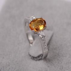 a ring with an orange and white stone in the center on top of sand,