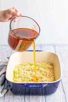 someone pouring sauce into a casserole dish with rice and vegetables on the side