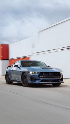 a blue mustang is driving down the road in front of a red and white building