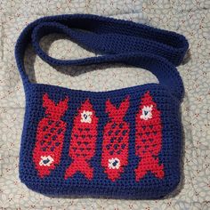 a blue crocheted bag with red fish on the front and bottom, sitting on a bed