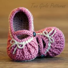 a pair of pink crocheted baby shoes sitting on top of a wooden table