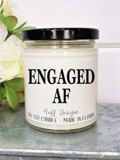 an engaged af candle sitting on top of a table next to flowers and a vase